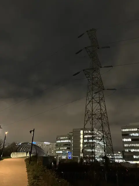 A moody electric pylon looking towards some office buildings